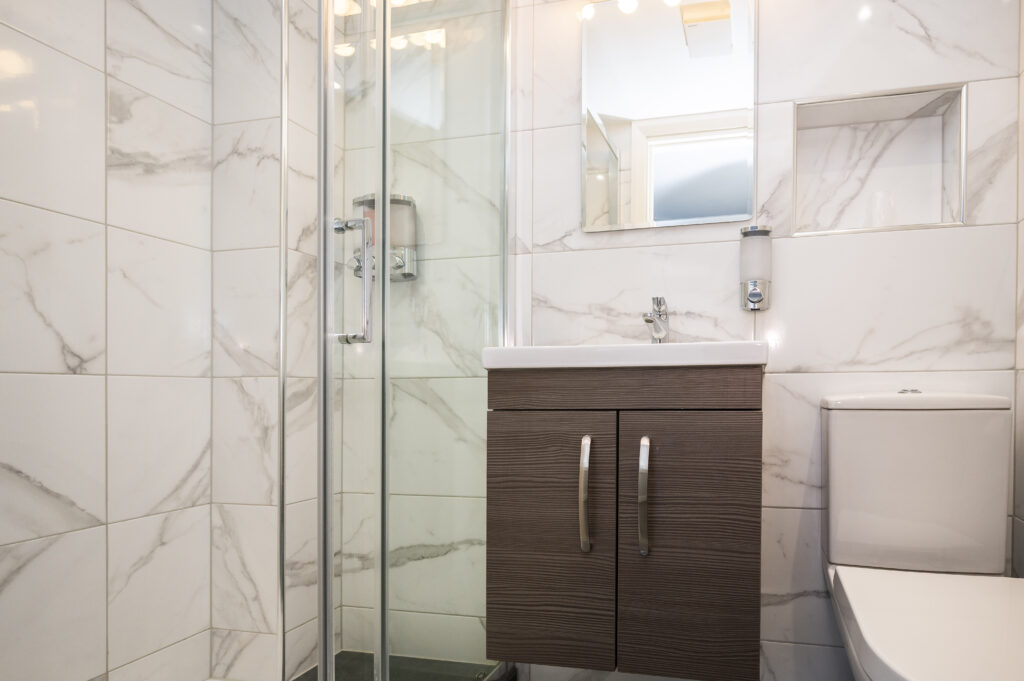 Modern bathroom with a glass shower door and wooden vanity, one of the elegant accommodation options at the Mentone Hotel