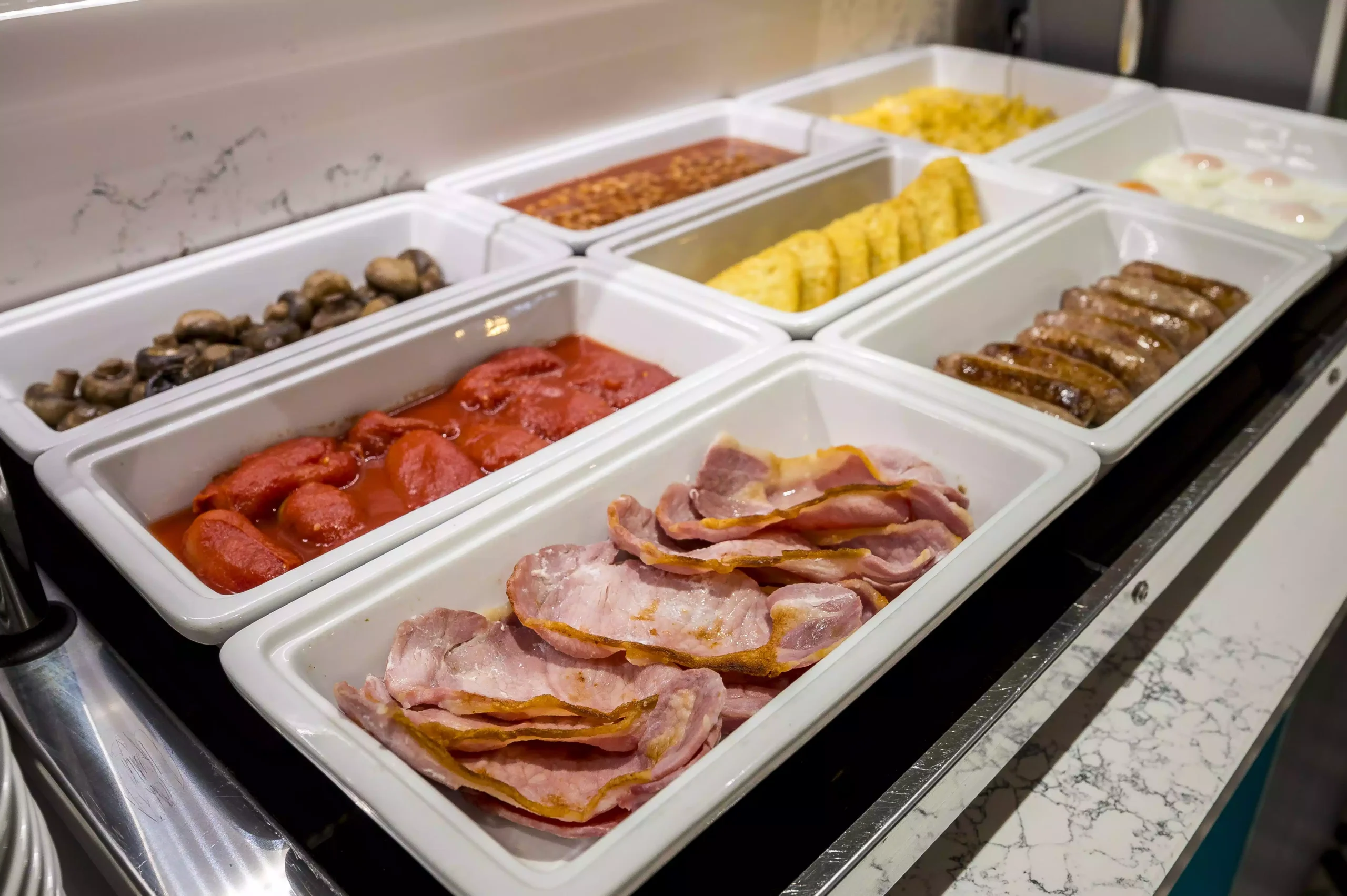 A tray with mushrooms, beans, tomatoes, bacon, sausages, hash browns, and fried eggs