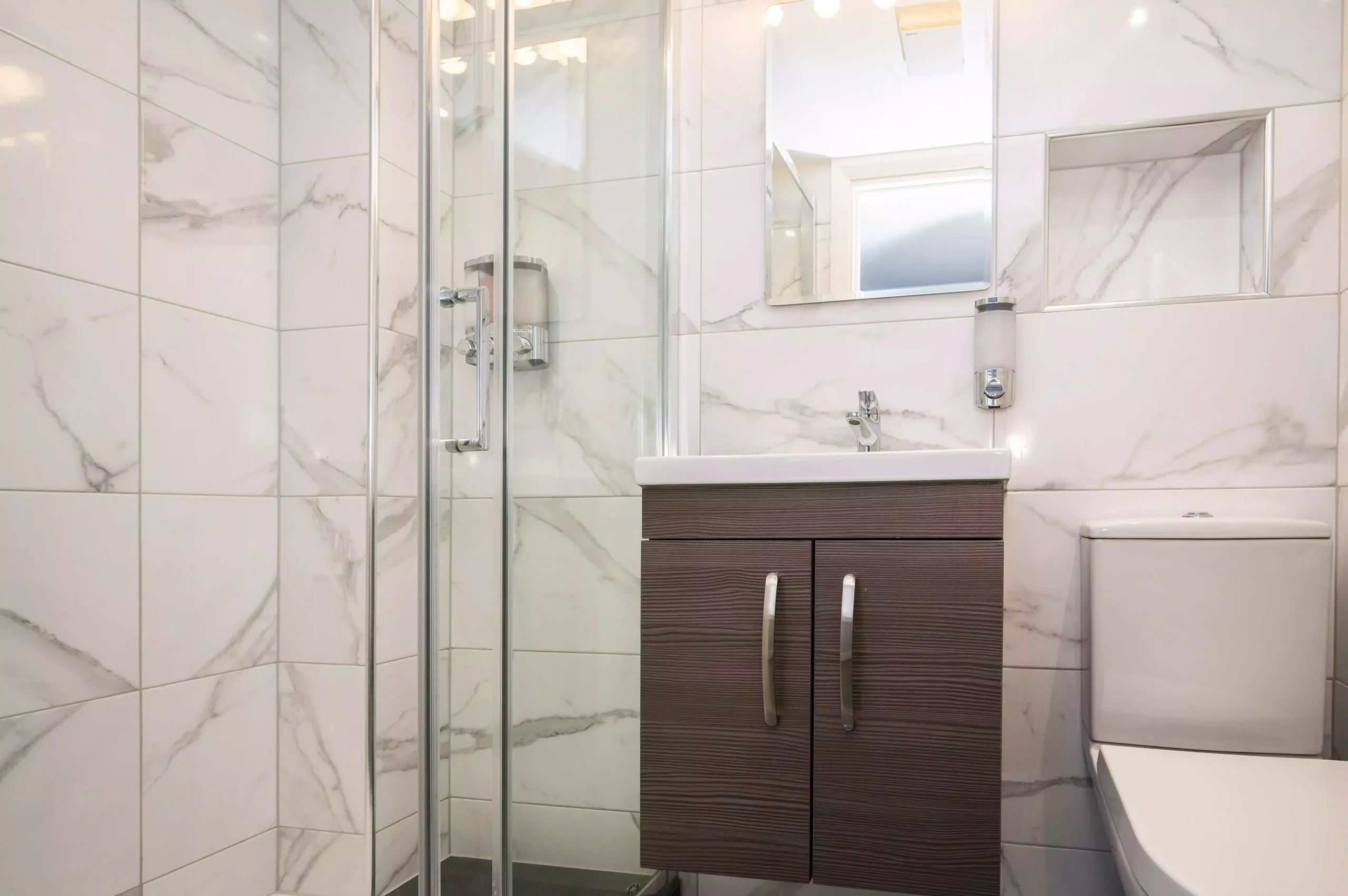 Modern bathroom with a glass shower door and wooden vanity, one of the elegant accommodation options at the Mentone Hotel