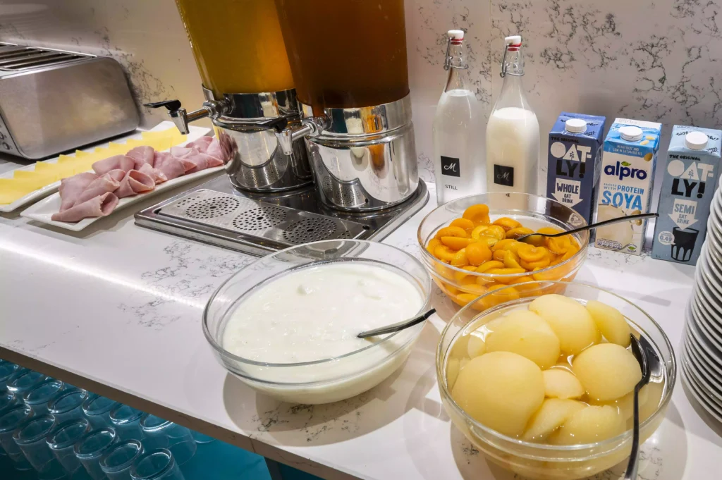 Mentone Hotel's breakfast buffet serving ham, juices, milk, oat and soy milk, yogurt, peach slices, and melon balls