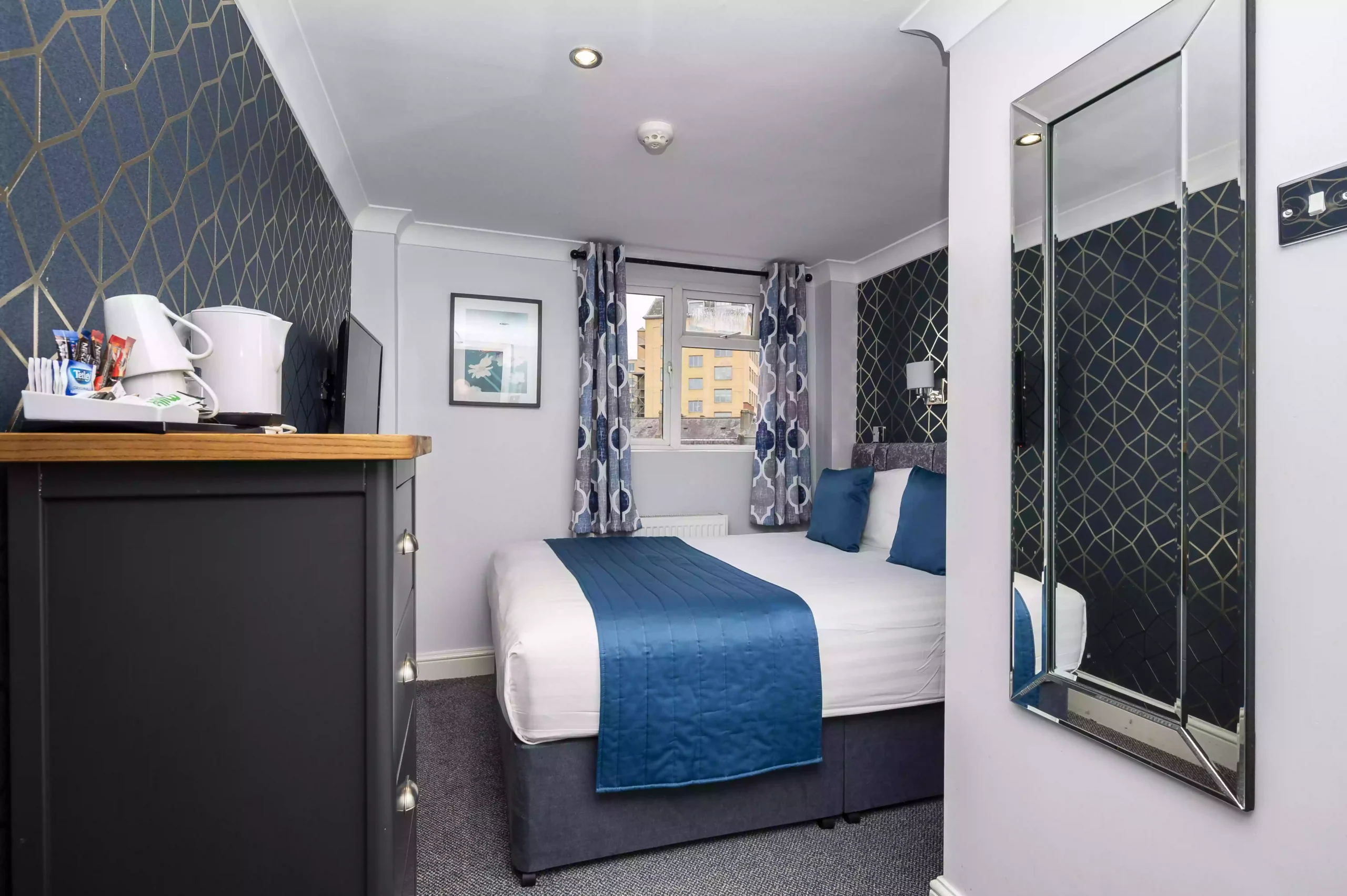Small double en-suite room at Mentone Hotel with a bed, dresser, and kettle